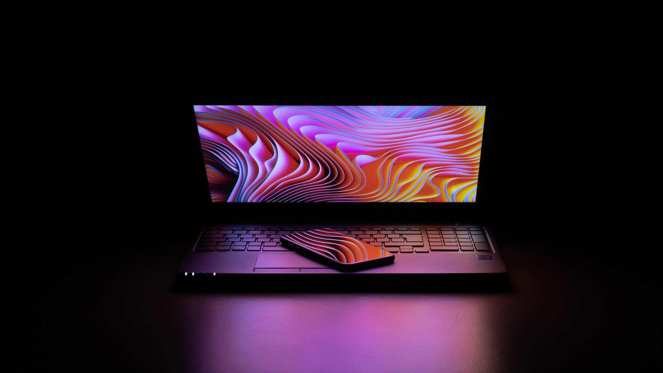 laptop half open with a screensaver showing and a phone on top of the keyboard